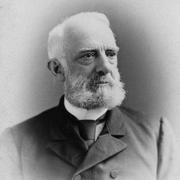 Black-and-white portrait of an older man with a full white beard and mustache, wearing a suit with a bow tie, facing slightly to the right against a plain background.